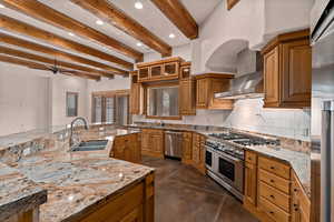 Kitchen featuring beamed ceiling, concrete floors, backsplash, light stone countertops, and high end appliances