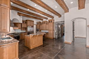 Kitchen with arched walkways, beamed ceiling, glass fronted cabinets, a kitchen island with sink, and high end appliances