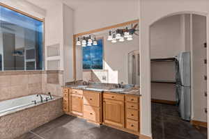 Primary full bathroom featuring double vanity, stacked washing machine and dryer, a spacious closet, a bath, and dark tile patterned floors