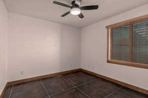 Empty second bedroom with ceiling fan and dark tile patterned flooring