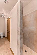 Full bath featuring tiled shower, a textured wall, a textured ceiling, and light tile patterned floors