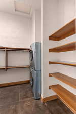 Primary closet with laundry area with finished concrete flooring, stacked washer and dryer, and a textured wall