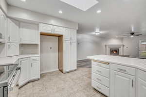 Kitchen featuring a tiled fireplace, white cabinets, recessed lighting, light countertops, and a skylight
