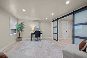 Home office featuring a barn door, light wood-style flooring, a textured ceiling, and recessed lighting