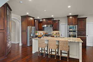 Two tone kitchen featuring arched walkways, a breakfast bar area, stainless steel appliances, a center island with sink, and two tone cabinets
