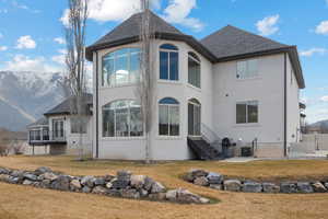 Rear view of house featuring a mountain view, roof with shingles, a yard, and stucco siding