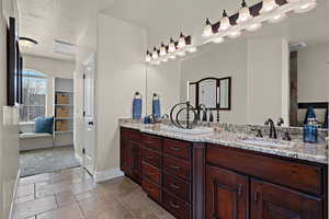Ensuite bathroom featuring double vanity, a textured ceiling, and stone tile flooring