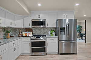 Kitchen featuring stainless steel appliances, white cabinets, light stone countertops, recessed lighting, and an office area