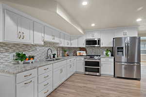 Kitchen featuring white cabinets, stainless steel appliances, light stone countertops, light wood-style flooring, and recessed lighting