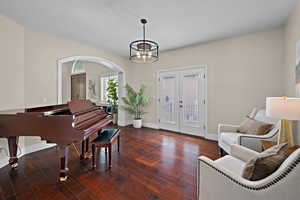 Living area featuring french doors, dark wood-style flooring, hanging lights, arched walkways, and a textured ceiling