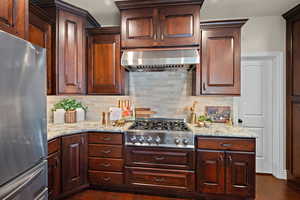 Kitchen featuring stainless steel appliances, light stone counters, dark wood-type flooring, and decorative backsplash