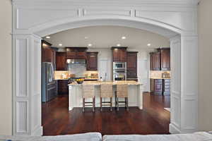 Kitchen featuring a breakfast bar, two tone cabinets, arched walkways, a kitchen island with sink, and stainless steel appliances