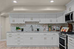 Kitchen featuring white cabinetry, stainless steel appliances, light stone counters, light wood-style flooring, and recessed lighting