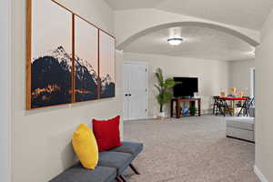 Living area with arched walkways, light carpet, and a textured ceiling
