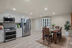 Kitchen featuring stainless steel appliances, recessed lighting, light wood-style floors, white cabinets, and light stone counters