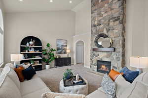 Carpeted living room featuring a stone fireplace, lofted ceiling, arched walkways, and recessed lighting