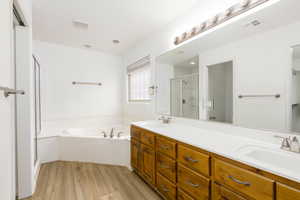 Bathroom featuring a shower stall, a bath, double vanity, and light wood-style floors