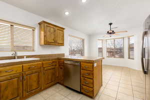 Kitchen featuring a peninsula, wood finish cabinets, tile counters, stainless steel appliances, and light tile patterned floors
