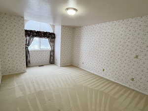 Empty room with a textured ceiling, light colored carpet, and wallpapered walls