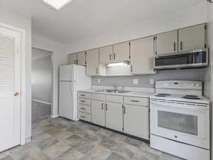 Kitchen with white appliances, light countertops, stone finish floors, and gray cabinetry