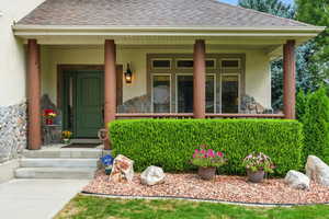 Doorway to property featuring roof with shingles, stone siding, stucco siding, and a porch
