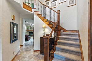 Stairs featuring a textured wall, a fireplace, a high ceiling, and ceiling fan