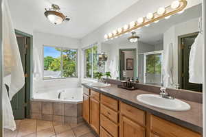 Bathroom featuring a tub with jets, a stall shower, double vanity, and light tile patterned floors