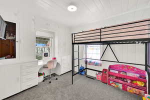 Carpeted bedroom with wooden walls and a desk
