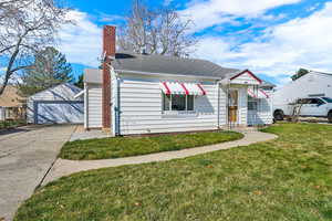 View of front of house with a front lawn, a garage, a chimney, an outdoor structure, and a shingled roof
