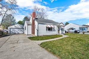 View of front of property featuring a front yard, a garage, an outbuilding, a chimney, and a shingled roof