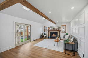 Open great room with wood look floor, decorative wood beams, and a cozy fireplace