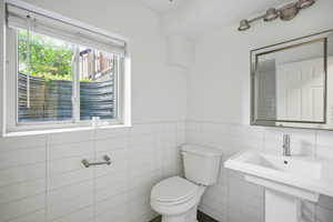 Basement bathroom with pedestal sink, toilet, updated lighting and mirror
