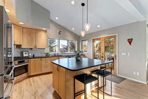 Kitchen with vaulted ceiling, a kitchen bar, stainless steel appliances, backsplash, and light wood-type flooring