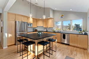 Kitchen with light wood finish cabinetry, lofted ceiling, stainless steel appliances, light wood-type flooring, and a kitchen bar