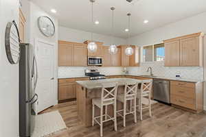 Kitchen with light wood finish cabinetry, a kitchen island, a breakfast bar area, stainless steel appliances, and decorative light fixtures
