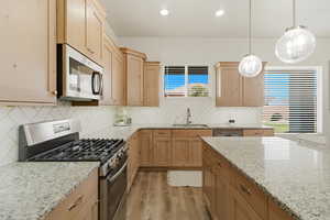 Kitchen with stainless steel appliances, light stone countertops, light wood-style floors, and light wood finish cabinets
