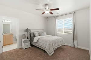 Bedroom featuring ceiling fan, light colored carpet, and ensuite bathroom