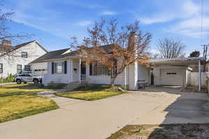 View of front facade with concrete driveway, a carport, a chimney, and an outdoor structure