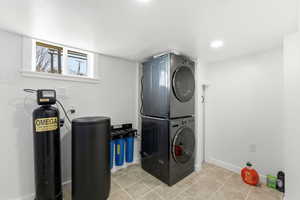 Laundry area with stacked washer and clothes dryer, light tile patterned floors, and recessed lighting