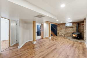 Below grade area featuring brick wall, a wood stove, light wood-style flooring, stacked washer / dryer, and recessed lighting