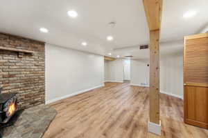Finished below grade area with light wood-type flooring, recessed lighting, and a wood stove