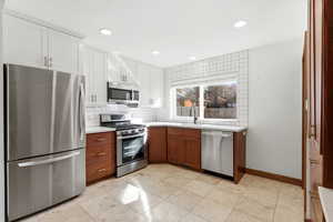 Dual tone kitchen with stainless steel appliances, light countertops, dual tone cabinetry, tasteful backsplash, and recessed lighting