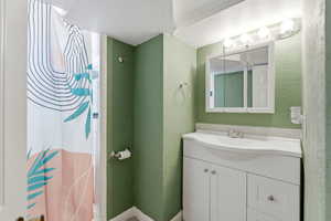 Bathroom featuring a textured ceiling, vanity, a shower with shower curtain, and a textured wall