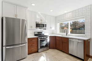 Kitchen with stainless steel appliances, dual tone cabinets, recessed lighting, decorative backsplash, and light tile patterned flooring