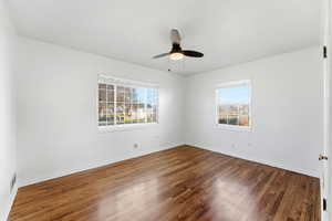 Spare room with dark wood-style flooring, plenty of natural light, and a ceiling fan