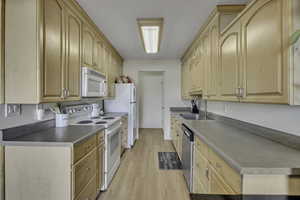 Kitchen featuring white appliances, light wood finish cabinets, and light wood finished floors