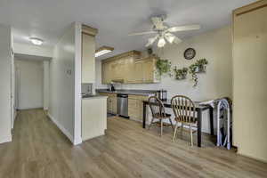 Kitchen featuring light wood finish cabinets, light wood-type flooring, a ceiling fan, dishwasher, and dark countertops