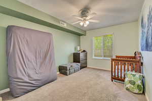 Carpeted bedroom with a ceiling fan and a crib