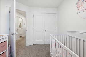 Bedroom with light colored carpet, a crib, and a closet