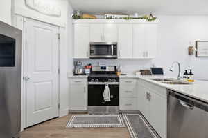 Kitchen with stainless steel appliances, white cabinetry, light wood-style flooring, and light stone counters